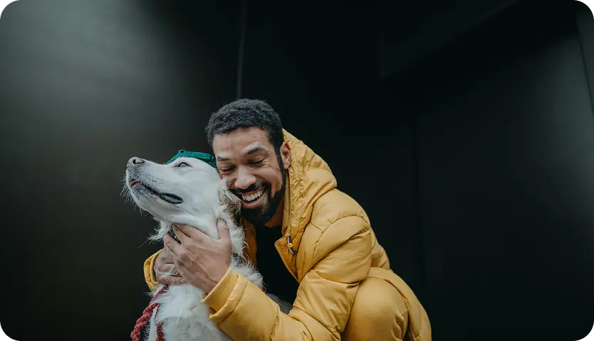 araffe man in yellow jacket hugging a white dog in a dark room